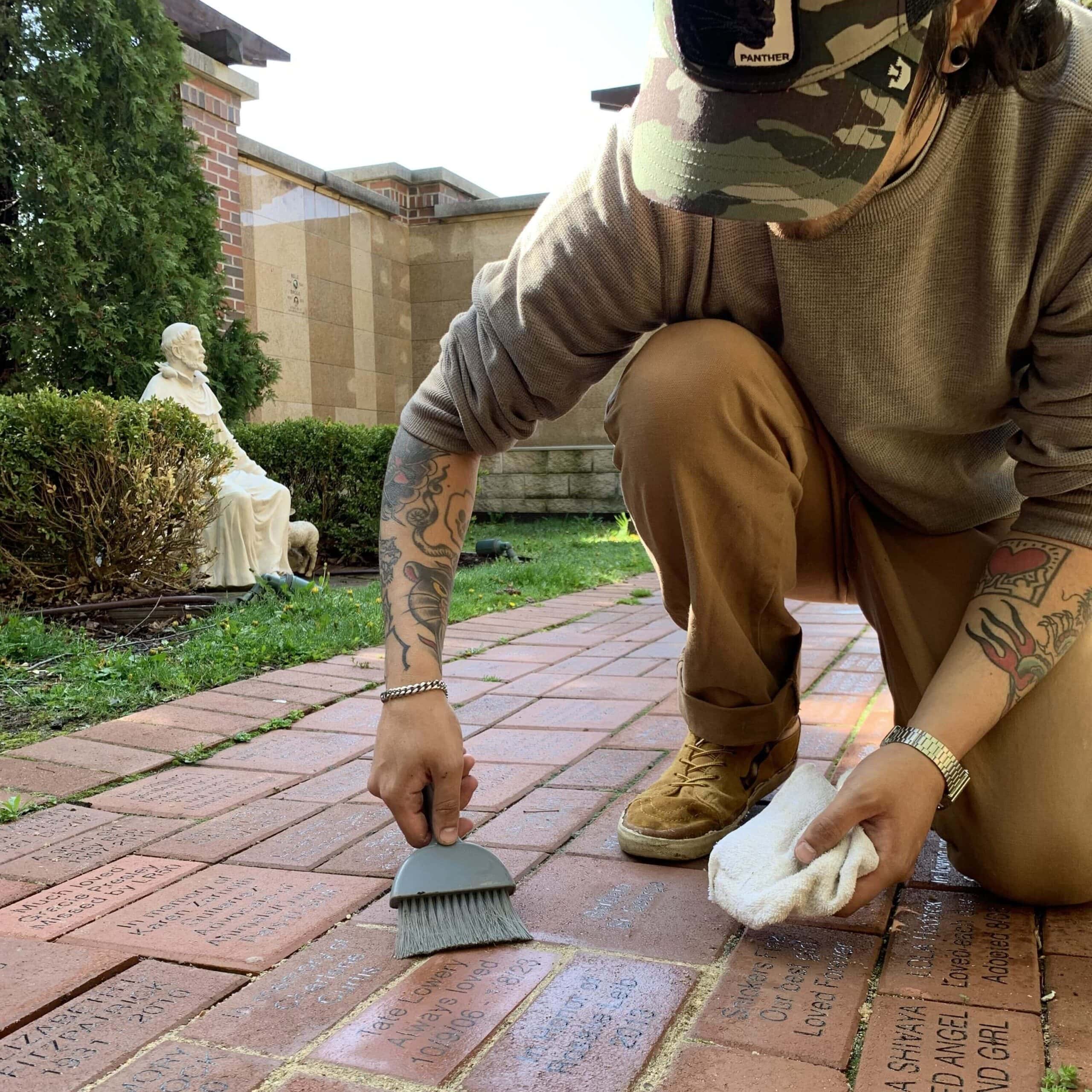 Man crouches down to install a memorial brick into a garden path