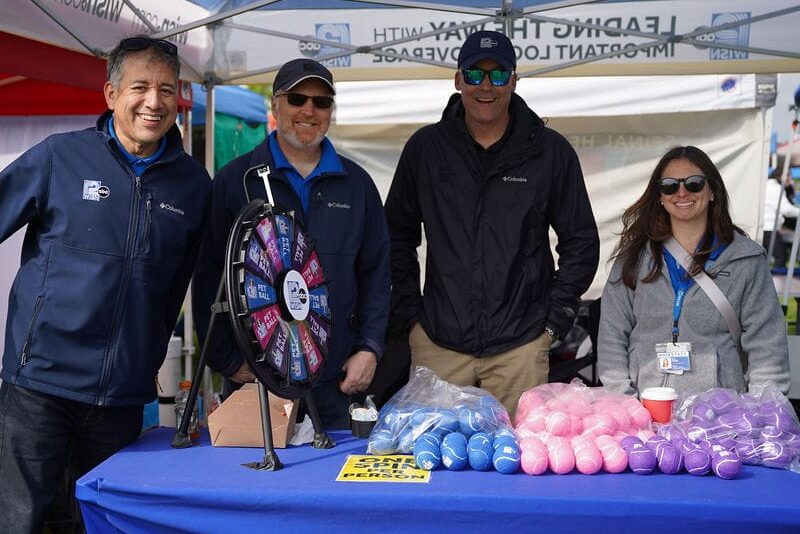 Four people stand smiling behind exhibitor table at festival