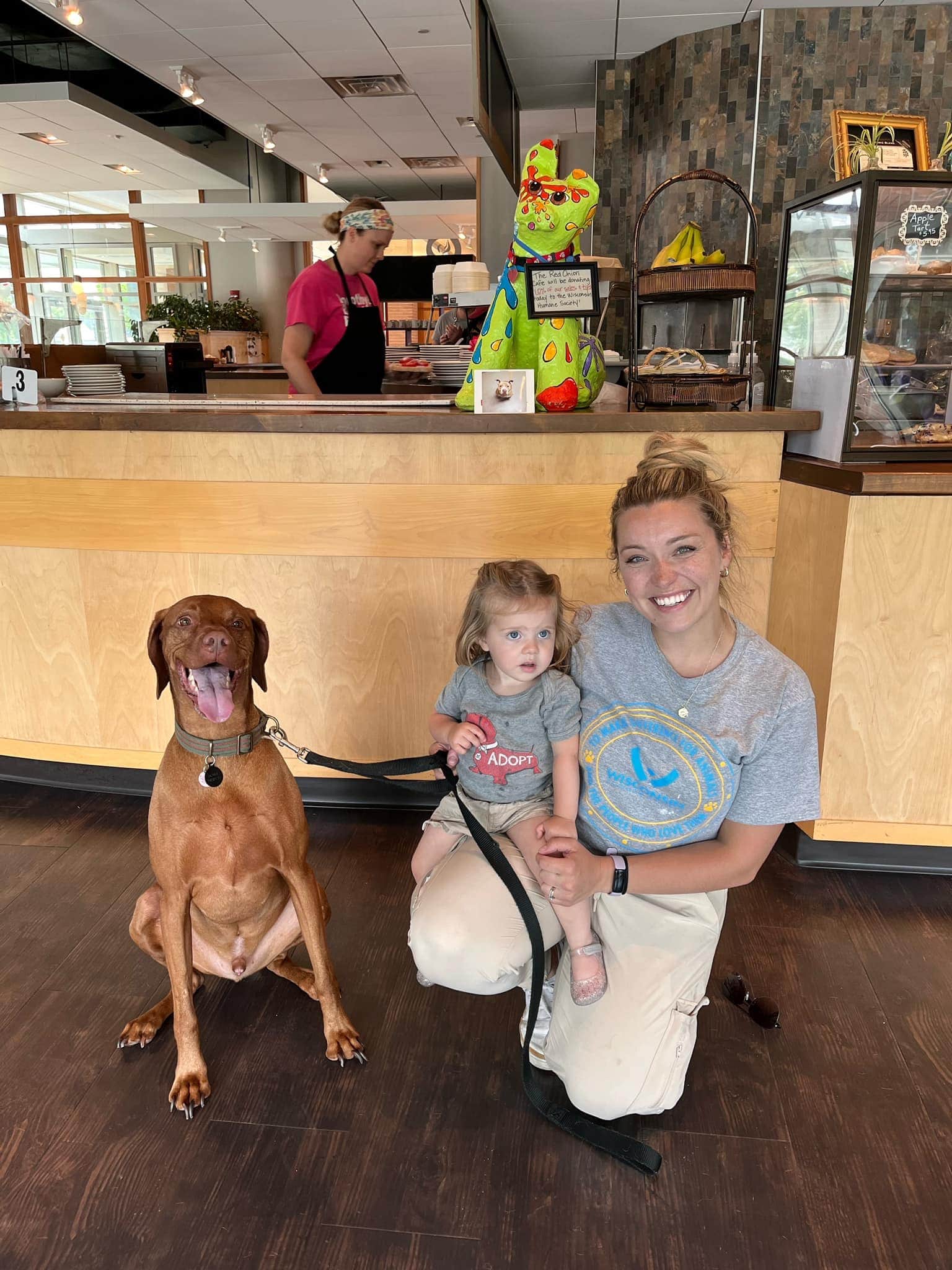 woman with child and dog smile in front of cafe counter