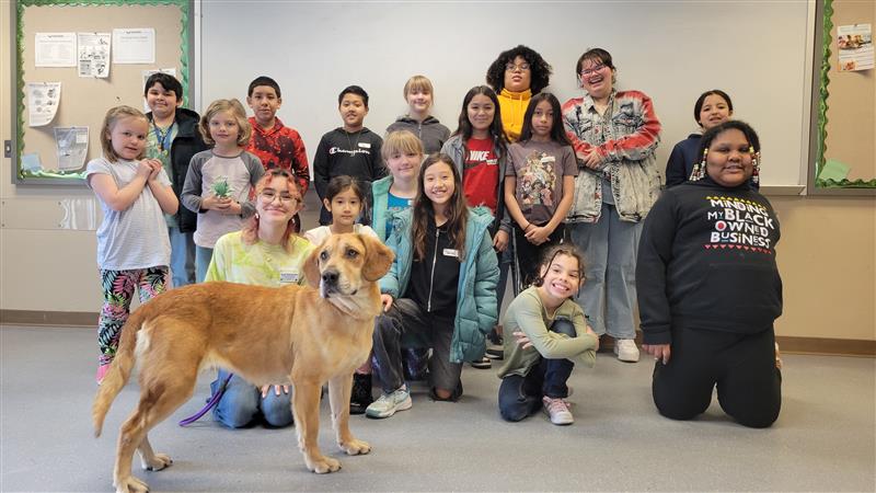 large group of kids smiles together with golden dog in front