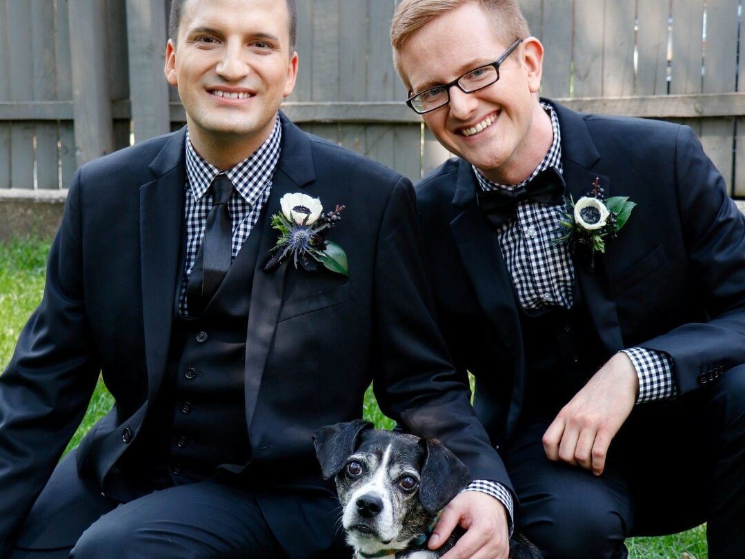 two men in suits kneel with dog