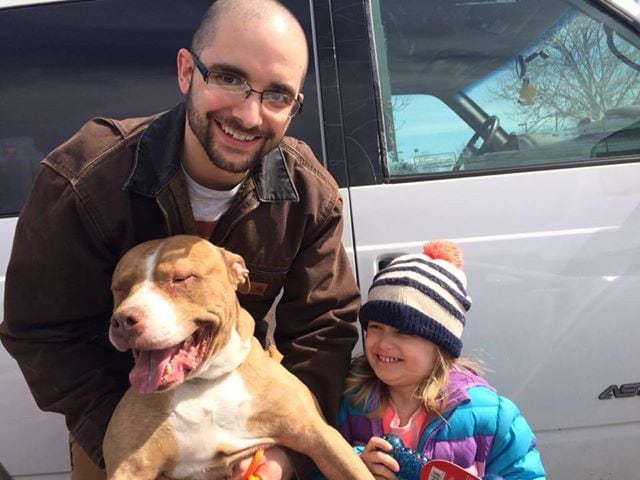 man and child stand next to vehicle with smiling dog